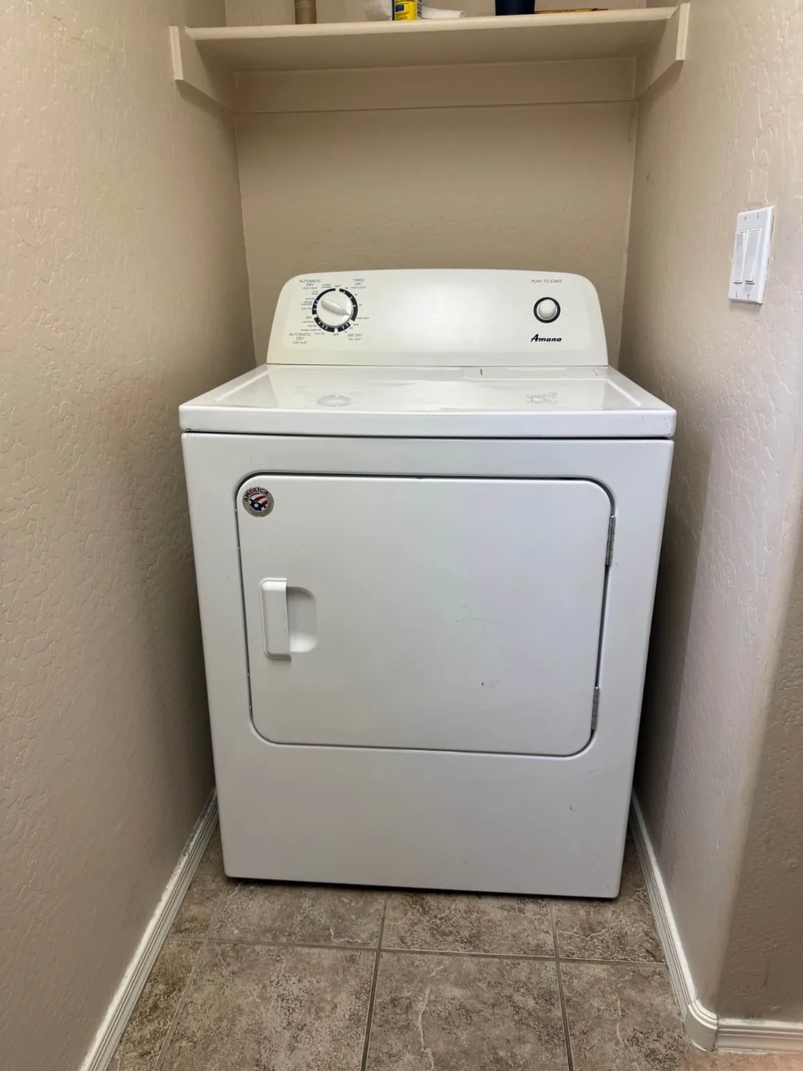 White Amana electric dryer photographed in a residential laundry alcove